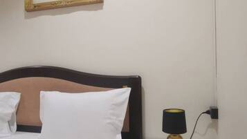 Una cama bien tendida con ropa blanca, un cabecero de madera y una mesita de noche con una lámpara.