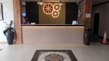 A reception desk with a patterned wall behind it, a modern chandelier, and a decorative rug in the lobby area.