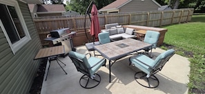 A patio with a table and chairs, a grill, and a wooden fence.