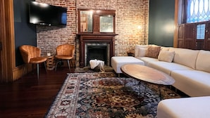 Ein Wohnzimmer mit Backsteinwand, Kamin, einer Chandelierleuchtre, einem Fernseher und einem gemusterten Teppich.