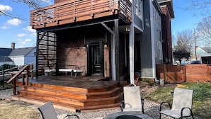 Ein modernes Haus mit überdachter Terrasse, Sitzgelegenheiten im Freien und einem Feuerkorb.