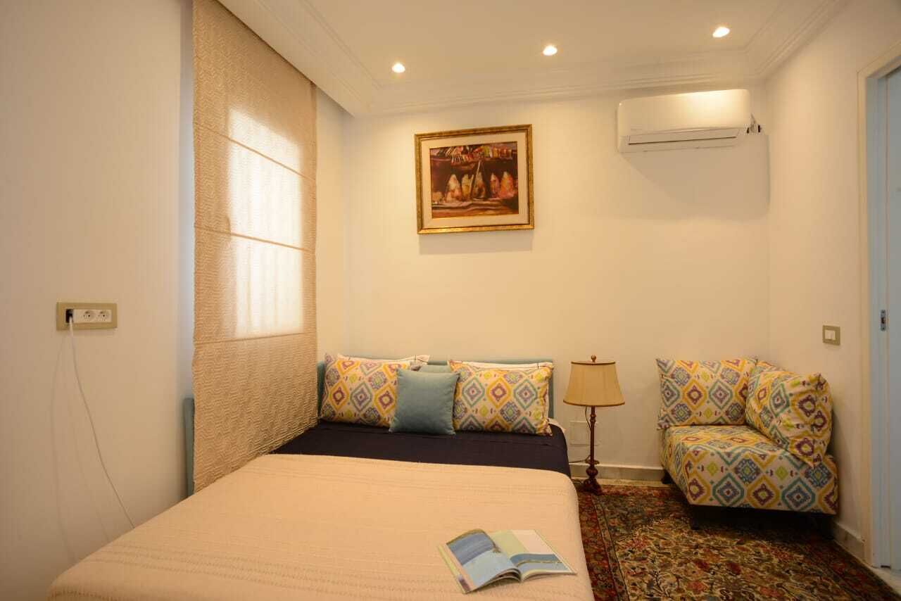 A hotel room with a bed, a sofa, a painting on the wall, and an air conditioner.