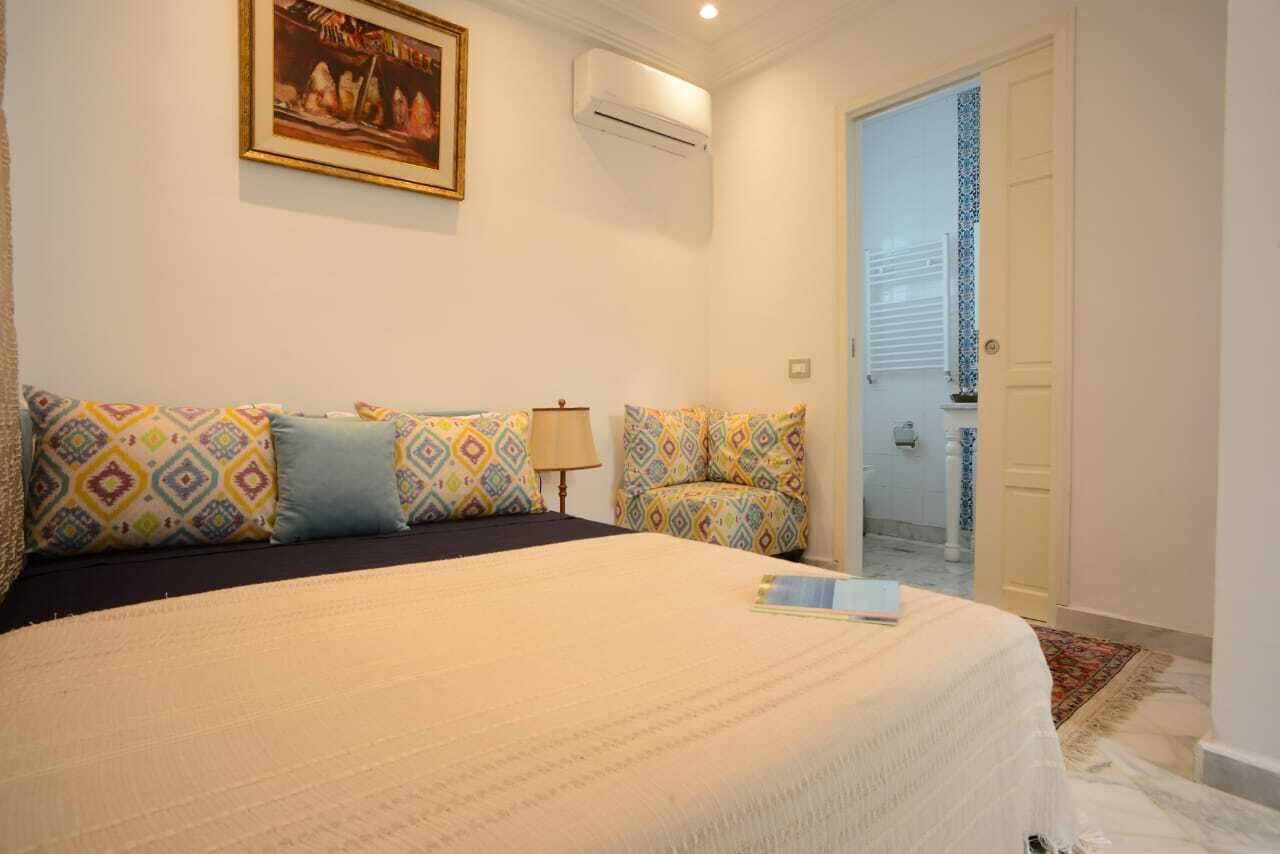 A hotel room with a large bed, patterned pillows, a bedside lamp, and a framed picture on the wall.