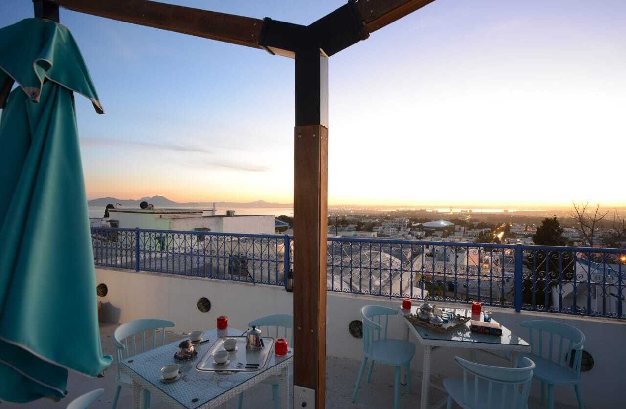 Un balcon avec une table dressée pour le dîner, offrant une vue sur le paysage urbain au coucher du soleil.