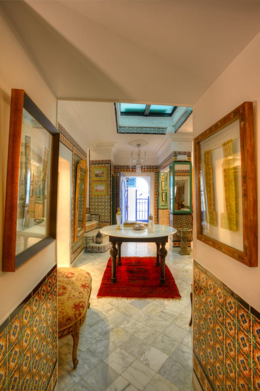 A hallway with patterned walls, a round table with a red rug, and a bench.