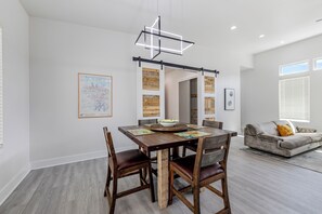 Un espace de repas moderne avec une table et des chaises en bois, un luminaire suspendu contemporain et un tableau représentant un paysage urbain accroché au mur.