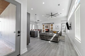 Un amplio espacio de sala con un ventilador de techo moderno, un sofá y un comedor con una cocina al fondo.