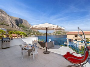 A terrace with a table, chairs, a grill, and a view of the sea and mountains. - Solemar Sicilia - Casa Margherita (Santa Flavia)