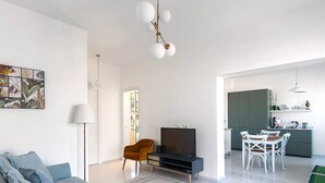 A modern living room with a sofa, a TV, and a dining area with chairs and a table.