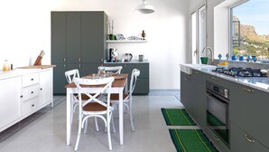 A modern kitchen with white cabinets, a dining table with chairs, a hanging light fixture, and a view of the outdoors through a window.