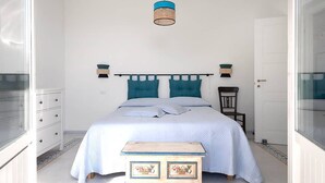 A bedroom with a bed, a small wooden chest, a hanging light fixture, and a door.