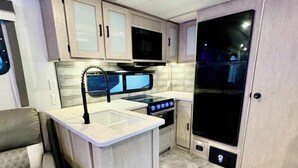 A compact kitchen with a central island, a stove, microwave, and cabinets. - RV in Lakeland, near Orlando & Ocala  (Lakeland)