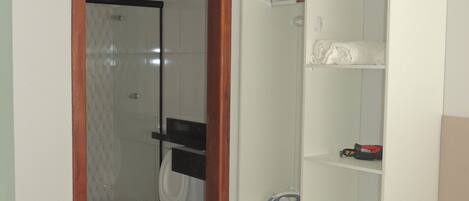 A bathroom with a toilet, a shower, and a white wardrobe with shelves.
