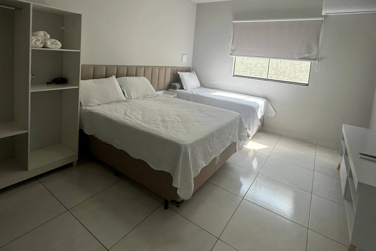 Un dormitorio con dos camas, un armario, una ventana con persianas y una lámpara en el techo.
