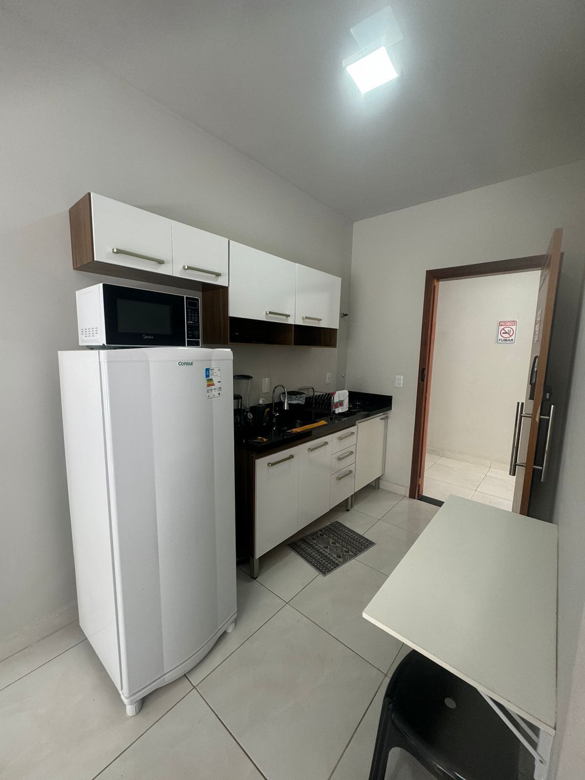 A compact kitchen with white cabinets, a microwave, a refrigerator, and a sink.
