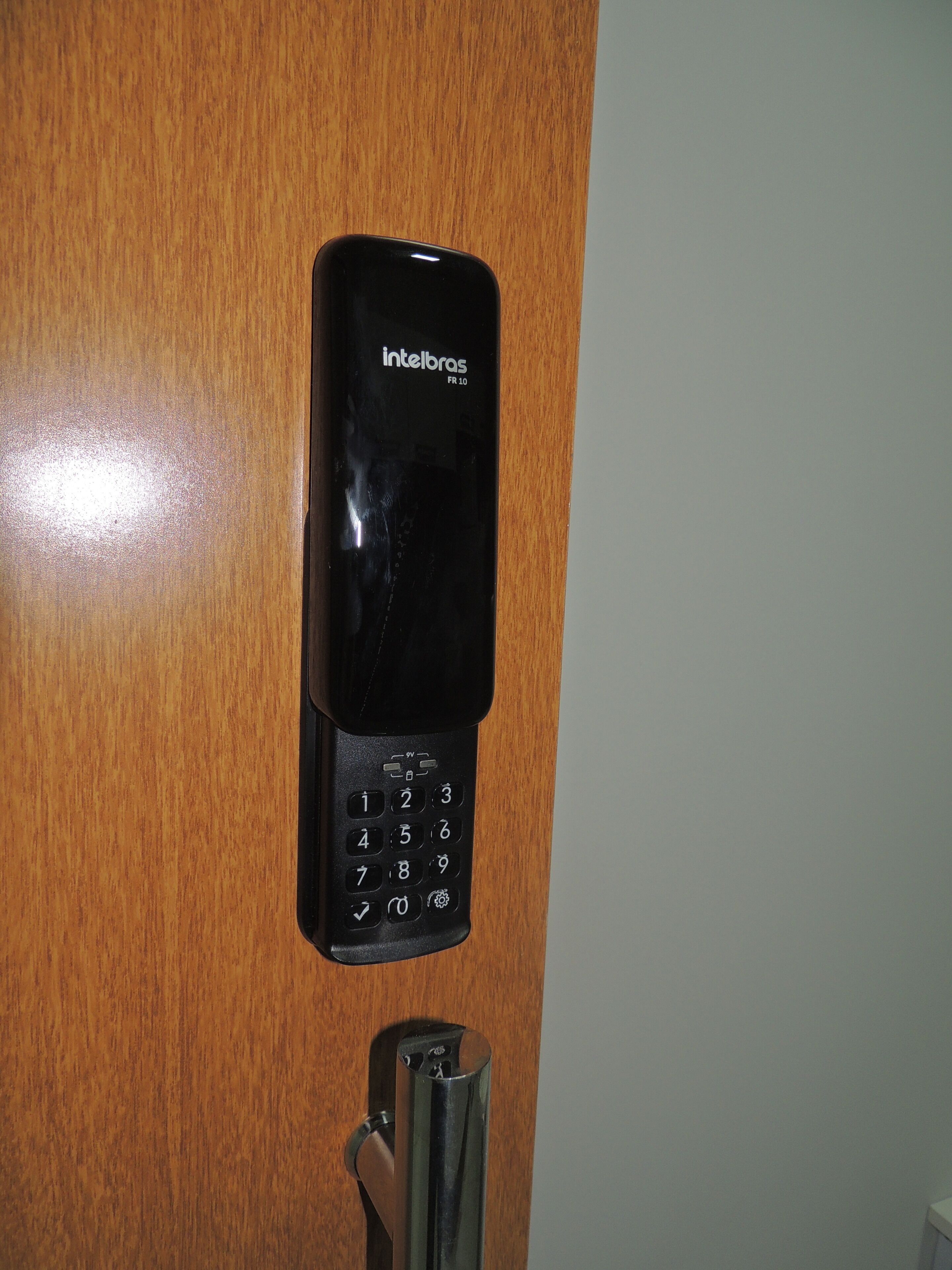 A black intercom device mounted on a wooden door, featuring a numeric keypad and a speaker grille.