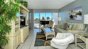 A living room with a sofa, armchair, and TV stand. There is a balcony with a view of the beach. - Sunny Siesta Key 1 Bed 1 Bath with Gulf Views  Steps to Beach (Siesta Key)