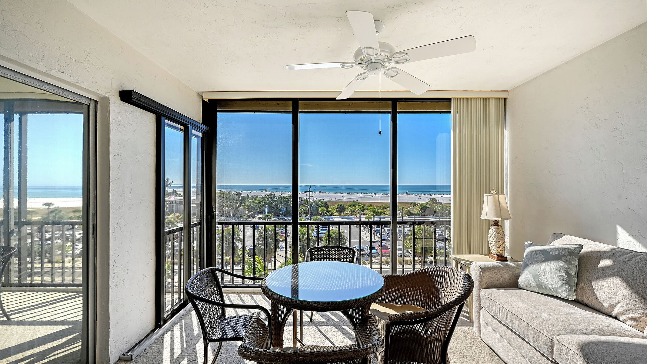 A balcony with a table and chairs, a ceiling fan, and a view of the beach and ocean.