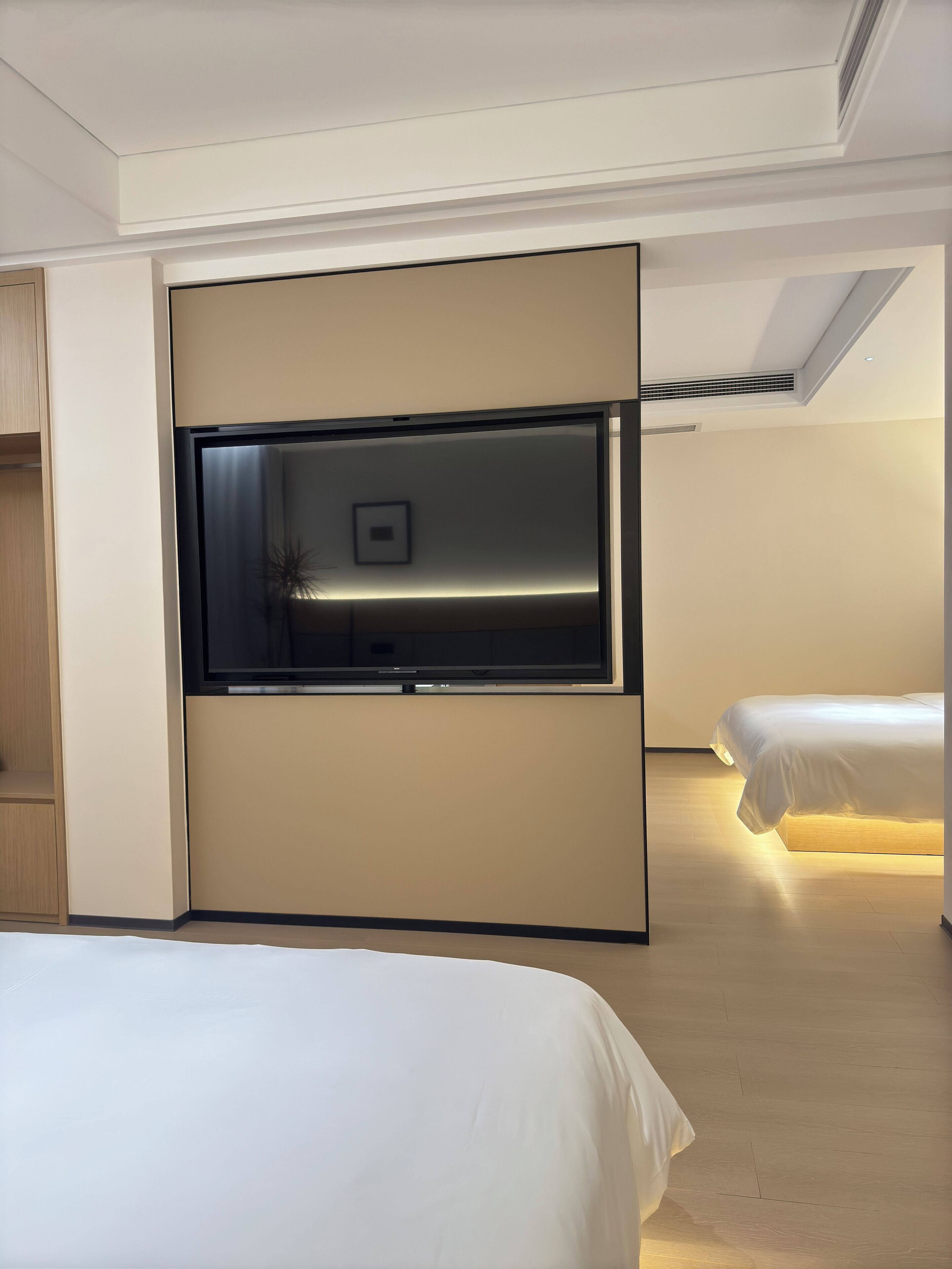 A modern hotel room with a bed, a built-in TV, and a bedside table.