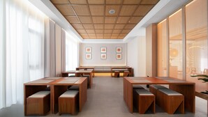 Ein moderner Konferenzraum mit Holztischen und -bänken, einer Decke mit Webmuster und gerahmten Kunstwerken an der Wand.