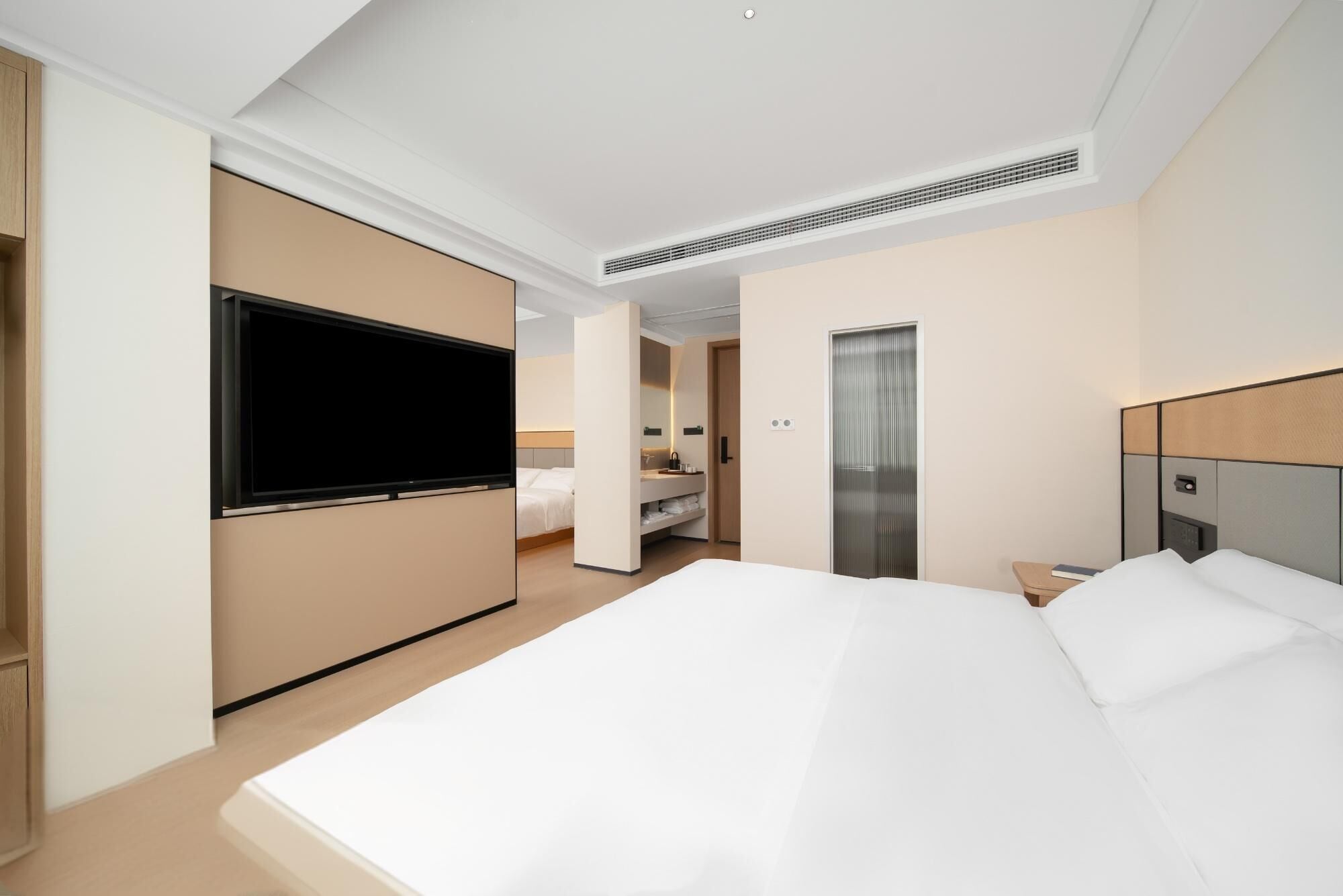 Moderni hotellihuone, jossa on suuri sänky, taulutelevisio, erillinen vaatehuone sekä kylpyhuone, jossa on suihku ja pesuallas.