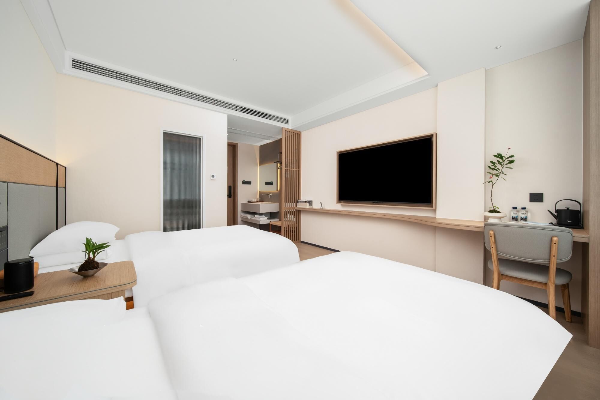A modern hotel room with a large bed, a desk with a computer, a TV, and a small plant.