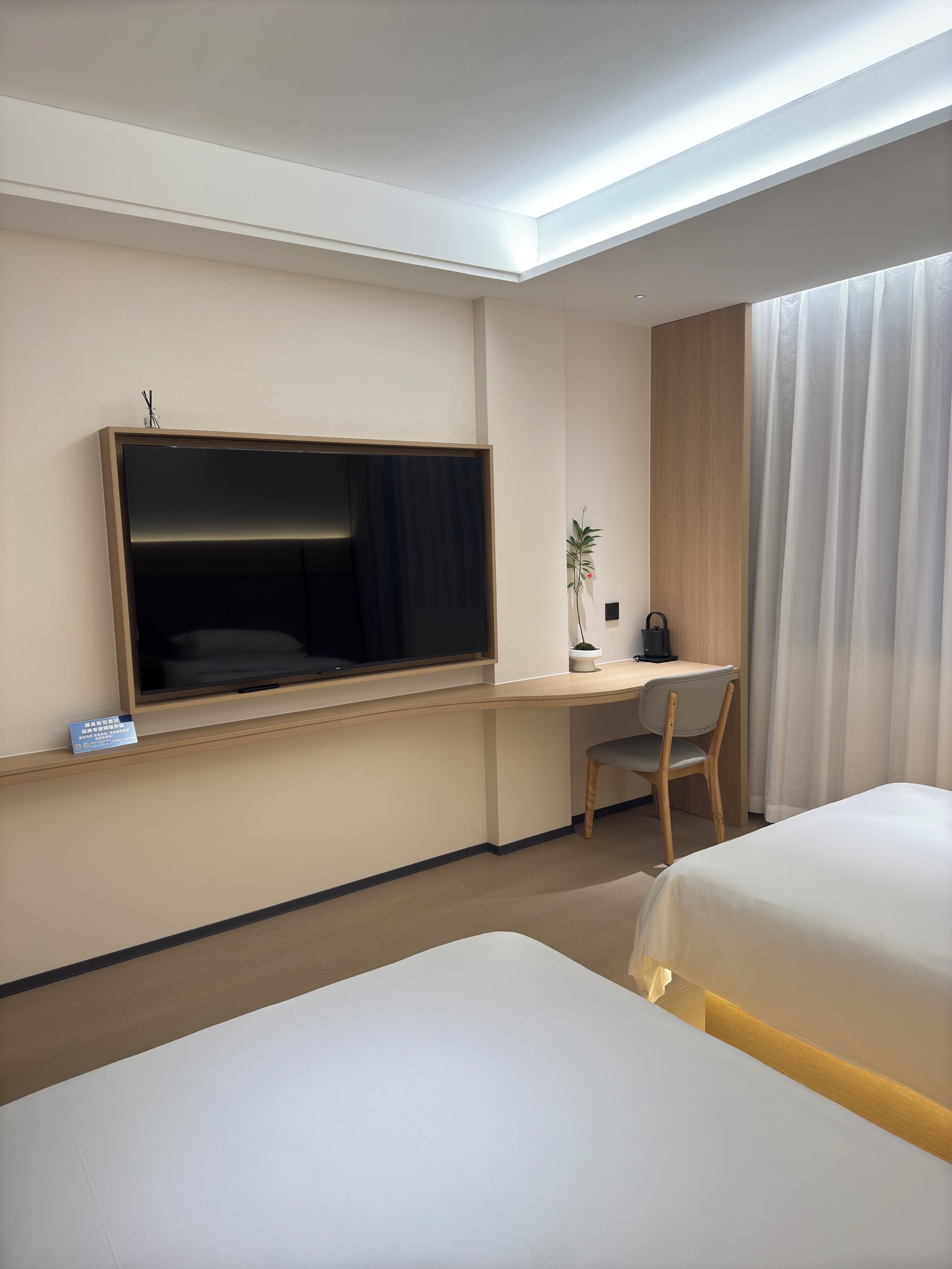 Habitación de hotel con cama, escritorio, silla, televisor y ventana con cortinas.