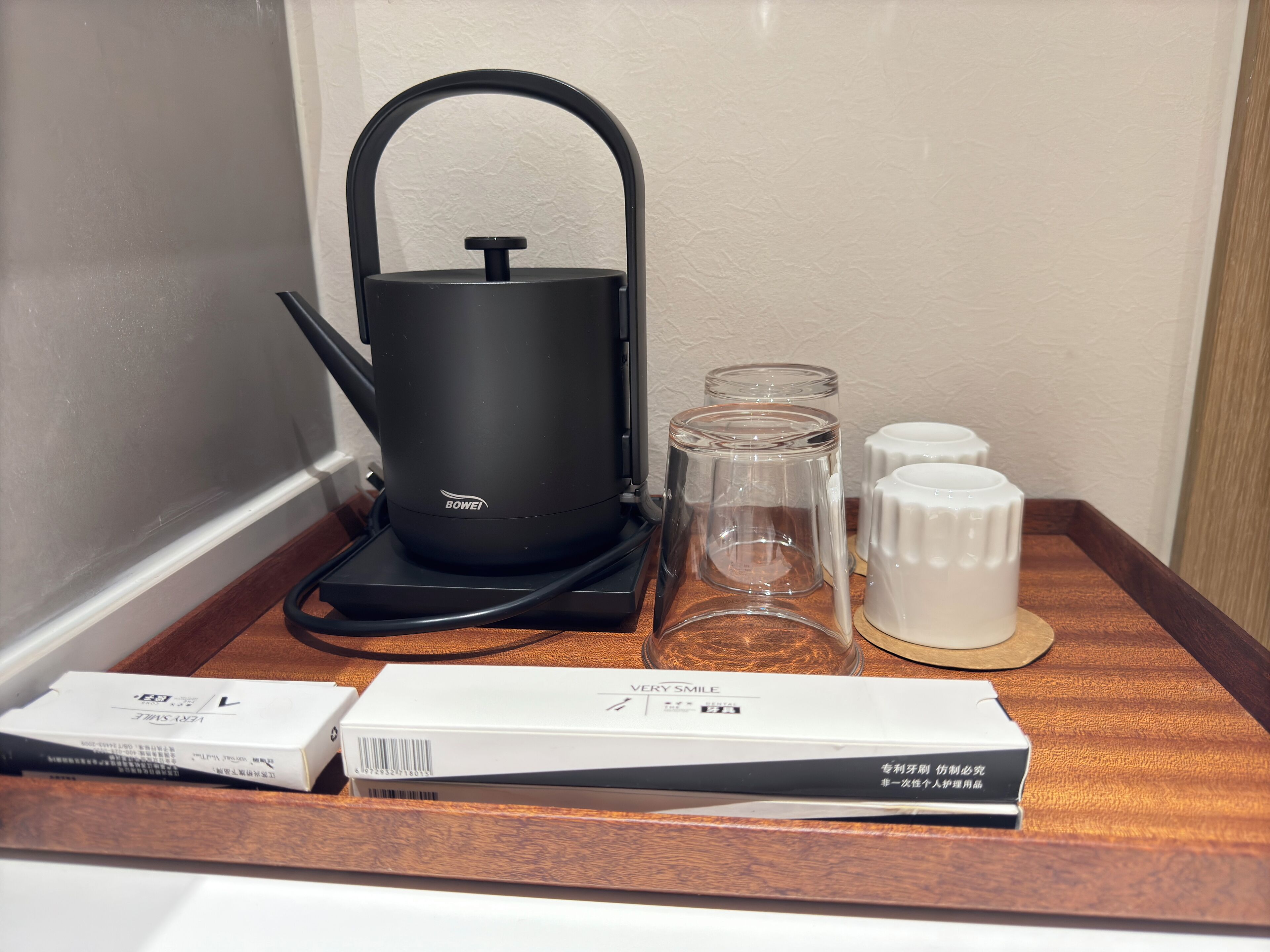 A coffee maker, a glass, and two white containers on a wooden tray.