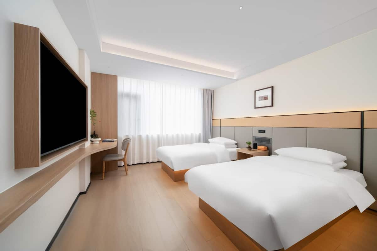 A hotel room with two beds, a desk, a TV, and a window with curtains.