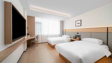 A hotel room with two beds, a desk, a TV, and a window with curtains.