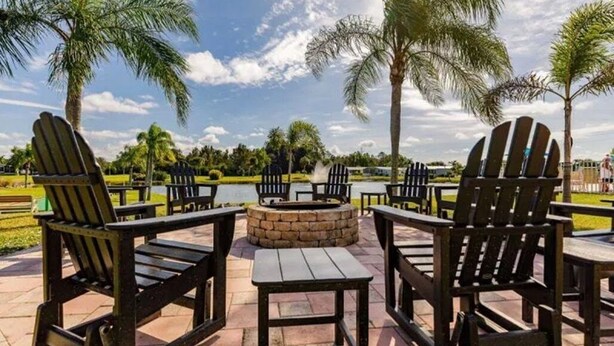 Outdoor seating with Adirondack chairs and a fire pit, surrounded by palm trees and a lake view. - Golfing, swimming and a friendly secure community (55+) - SEASONAL (30days+) (North Fort Myers)