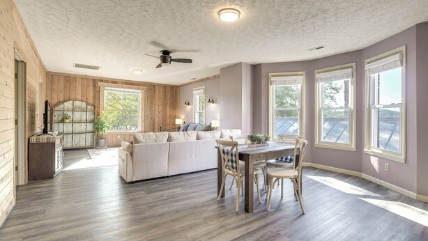 Un vaste espace de vie doté d’un plancher en bois, d’un canapé blanc, d’une table à manger avec des chaises et de grandes fenêtres laissant entrer la lumière naturelle.