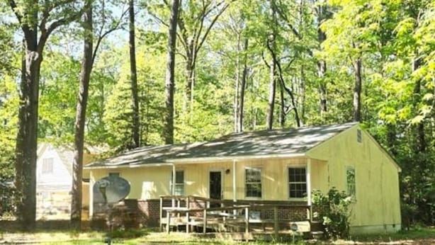 A single-story yellow building with a porch, surrounded by trees in a wooded area.