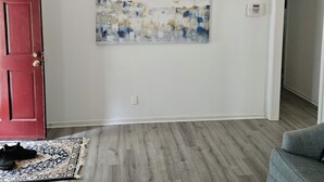 A room with a red door, a gray sofa, a patterned rug, and a wall-mounted abstract painting.