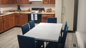 A compact kitchen with wooden cabinets, a white stove, and a refrigerator. There is a dining table with blue chairs.