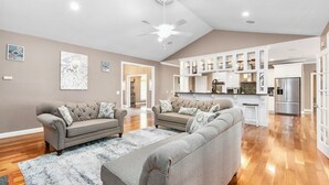 A spacious living room with a large sectional sofa, a ceiling fan, and a kitchen area with white cabinets and stainless steel appliances. - Spacious & Private Retreat Near Downtown & NC Zoo! (Asheboro)