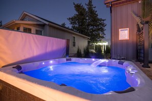 An outdoor hot tub with a blue-lit interior, surrounded by a wooden deck and a house in the background.