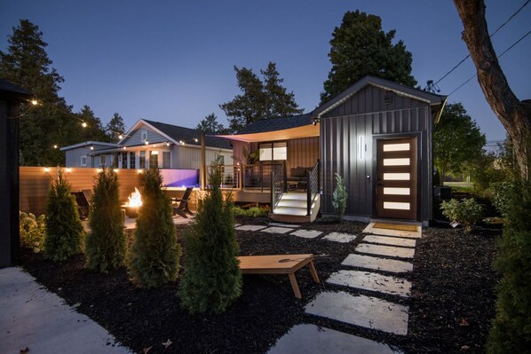A modern house with a well-lit patio, a small wooden deck, and a metal shed.