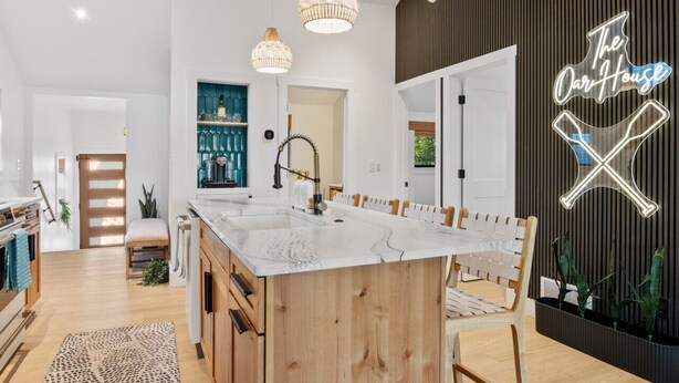 Une cuisine moderne dotée d’un grand îlot central, de luminaires suspendus et d’un néon affichant l’inscription « The Oak House ».