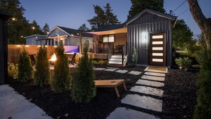 Une maison moderne dotée d’un patio bien éclairé, d’une petite terrasse en bois et d’un abri de jardin en métal.