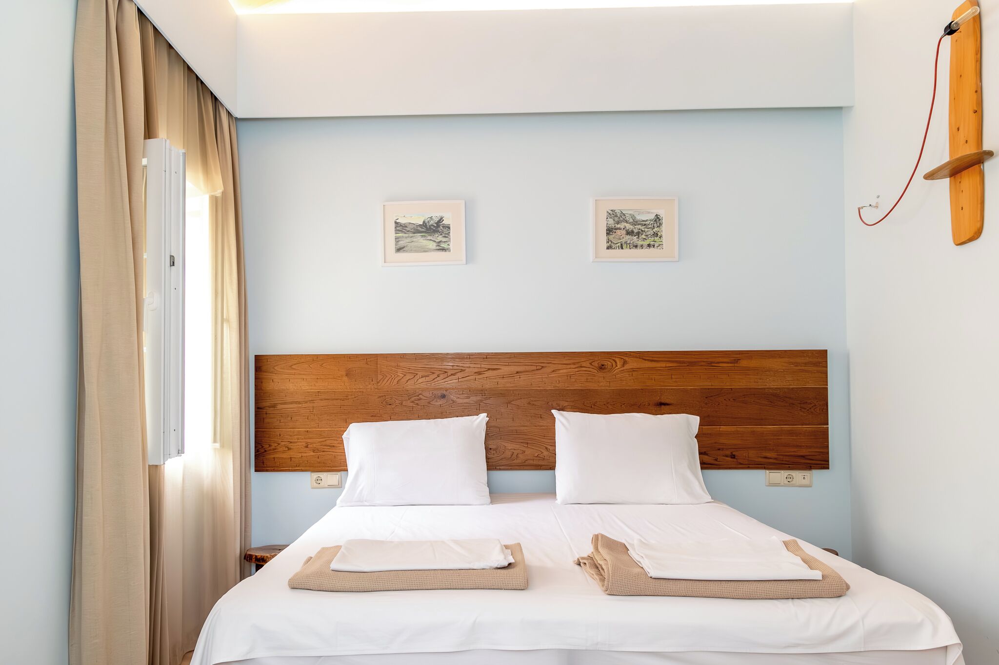A neatly made double bed with white linens, a wooden headboard, and two framed pictures on the wall.