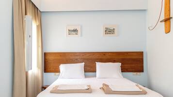 Una cama doble bien hecha con sábanas blancas, cabecera de madera y dos cuadros en la pared.