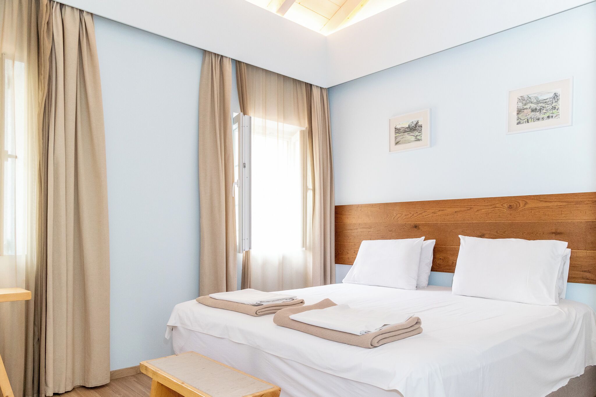 Une chambre d’hôtel avec un grand lit, deux oreillers, une tête de lit en bois et un banc.