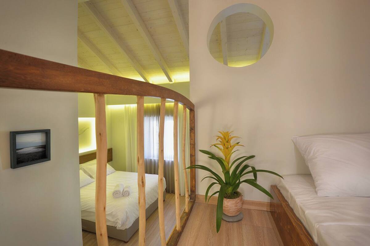 A bedroom with a wooden ceiling, a bed, a potted plant, and a wall-mounted mirror.