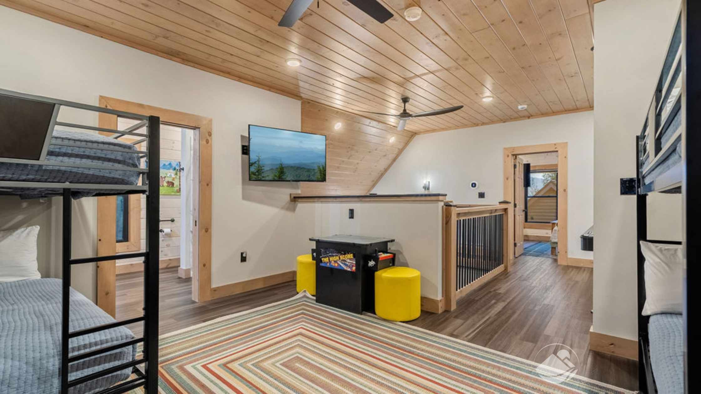 Un dormitorio tipo loft acogedor con literas, ventilador de techo, televisor y una pequeña mesa de juegos.