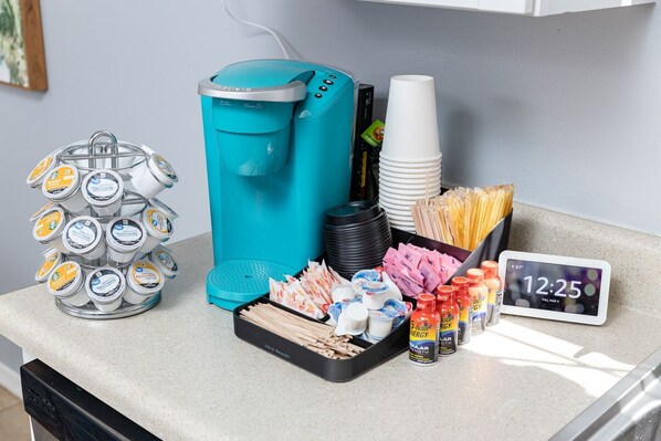 A breakfast setup with a coffee maker, stacked cups, condiments, and a clock.