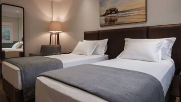 A hotel room with two beds, a large mirror, a lamp, and a painting of a bridge over water.
