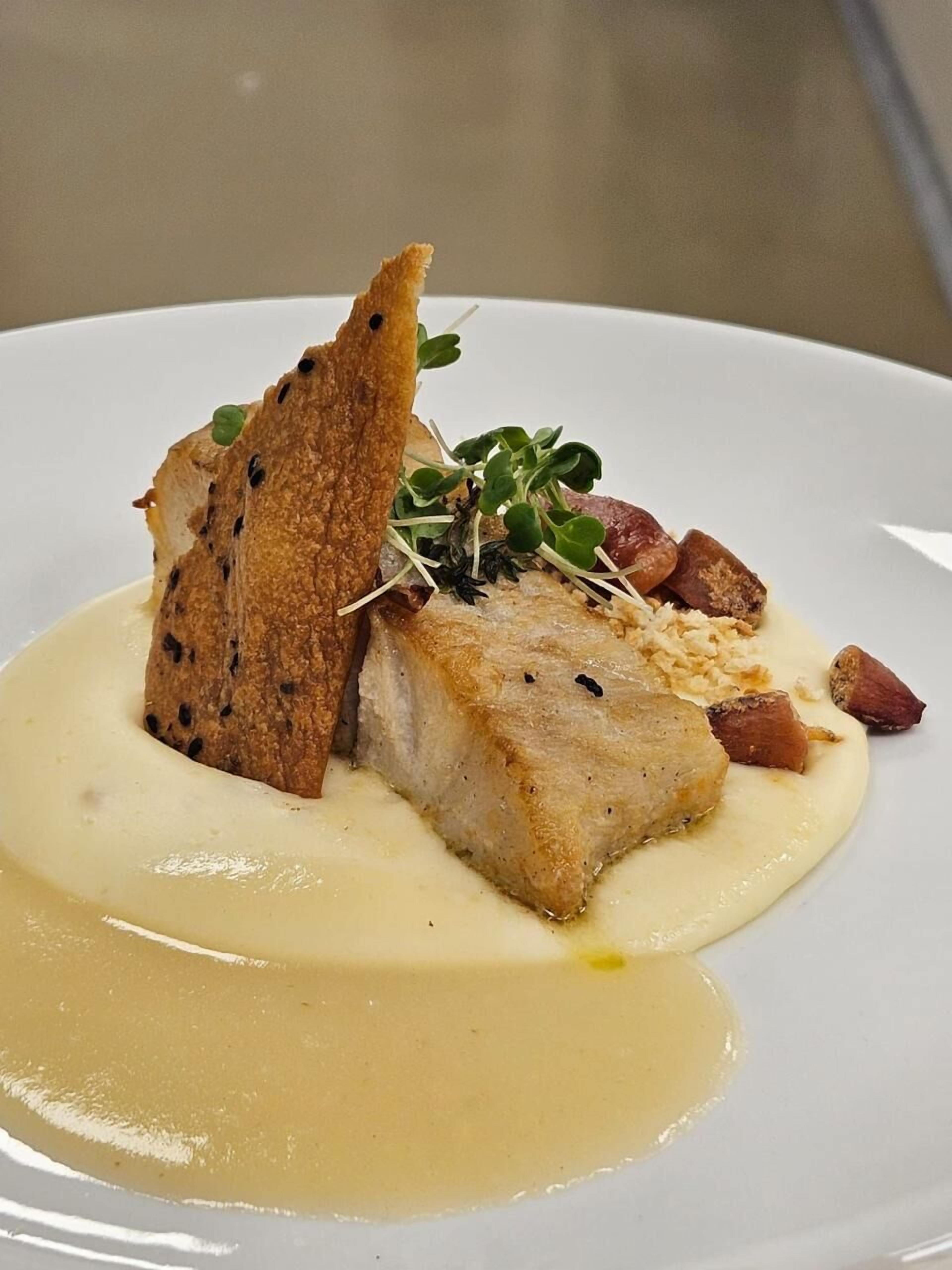 A dish with a piece of fish, bread, and greens on a white plate.