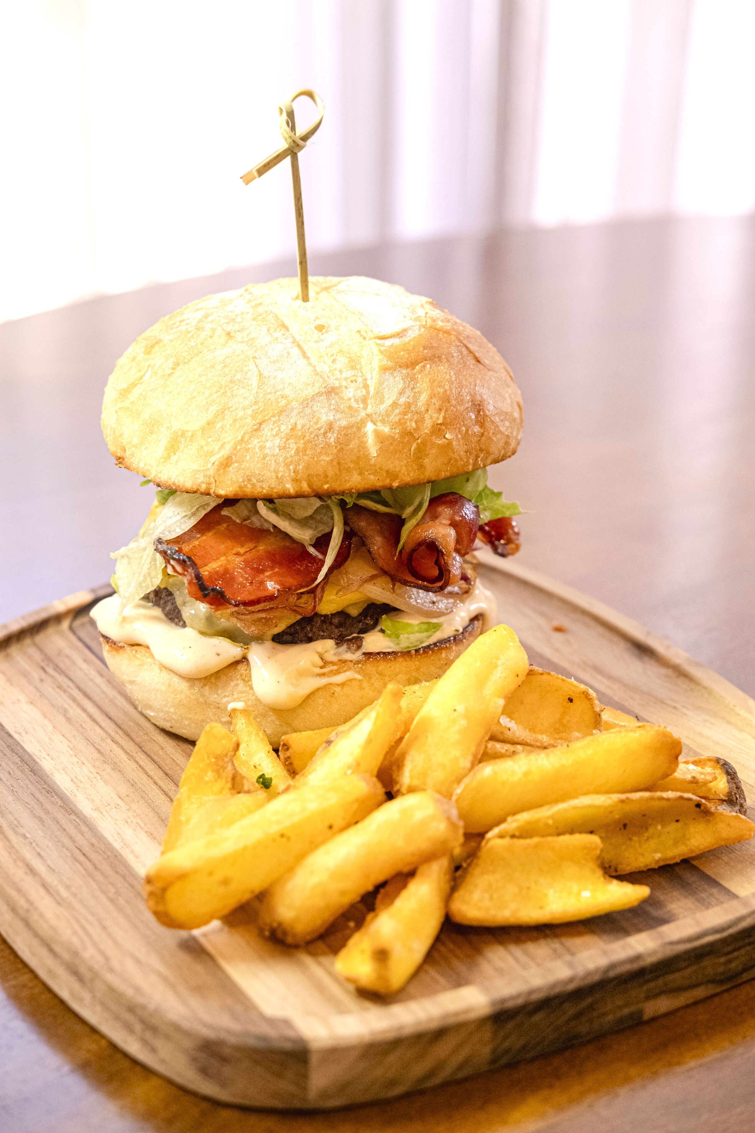 Una hamburguesa con tocino, lechuga y una porción de papas fritas sobre una tabla de madera.