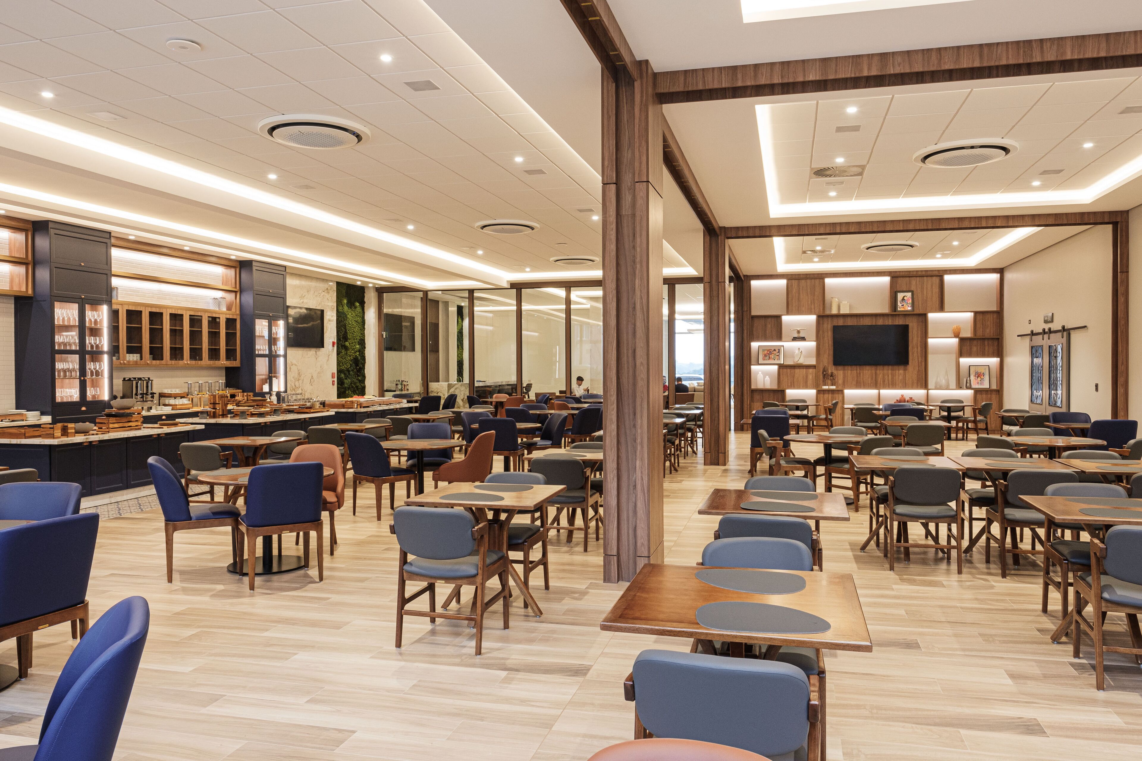 Um amplo hall de hotel com diversas áreas de estar, uma coluna central e um bar com televisão.